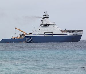 A blue and white ship sits offshore on a steady blue sea