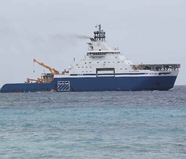 A blue and white ship sits offshore on a steady blue sea