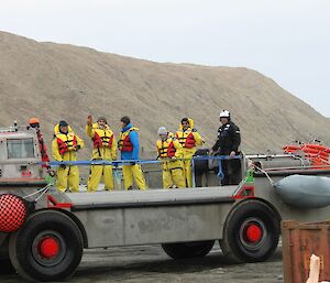 A group of people in yellow survival gear stand on the back of land and water transporter