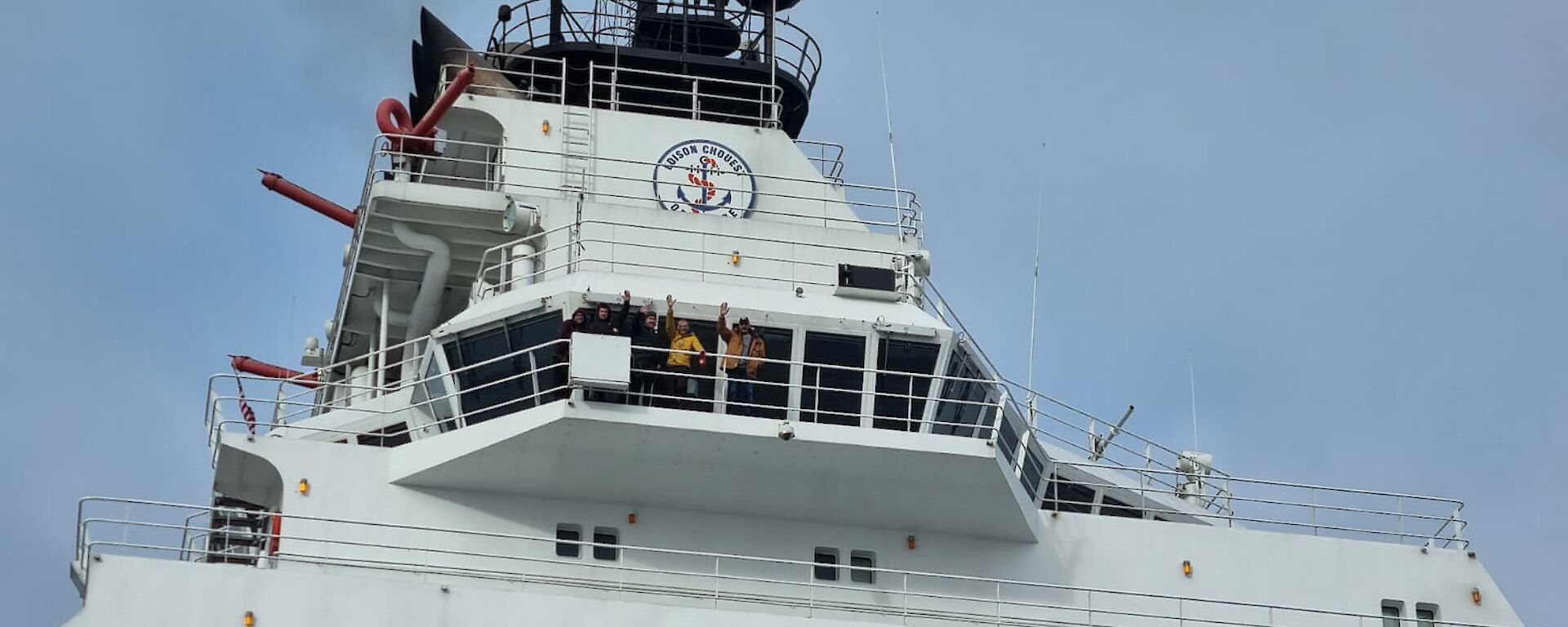 A group of people wave from a top deck of a ship