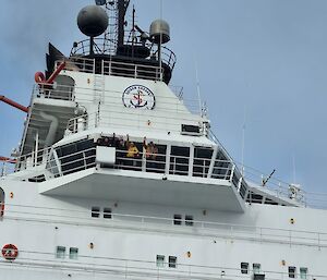 A group of people wave from a top deck of a ship