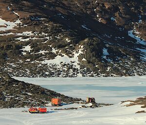 A red vehicle is stopped near two huts in a snowy landscape