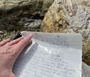 A piece of paper with a hand holding it flat is bright against the rocky background