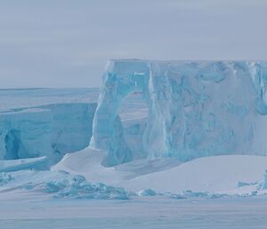 A large iceberg glows white and blue under a light sky