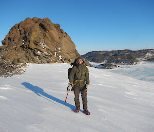 A man standing on the snow in front of a large boulder
