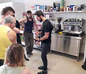 A man standing in front of a coffee machine with the portafilter in his hand, explaining coffee making to a group of onlookers