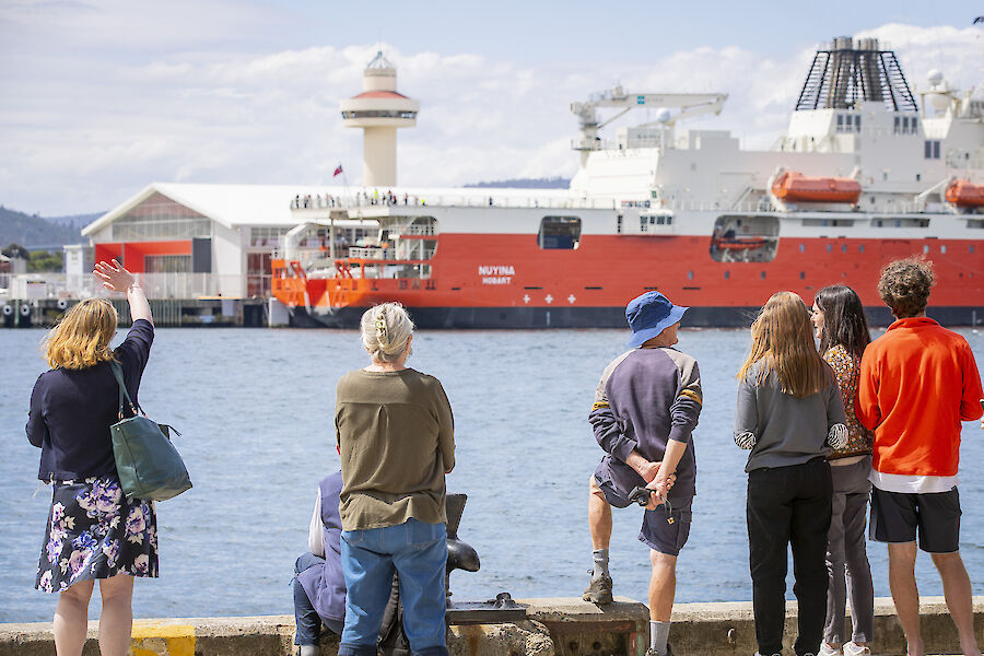 A group of well wishers wait on a dock with a ship across the water readying to depart