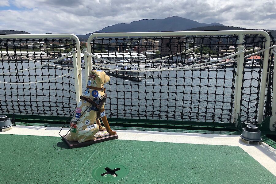 A plastic guide dog sitting at the rear of a ship looking out towards Hobart