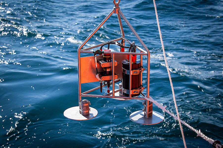 A hydrophone instrument dangles on a winch, just above the water.