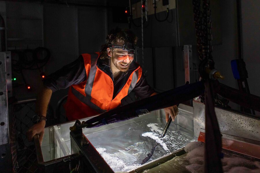 A man with a head torch on looks in to a container filled with water