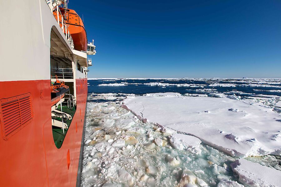 Looking down the side of a ship as it sails through bits of floating ice