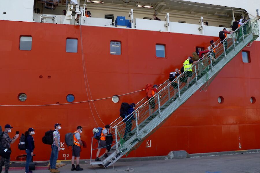 A gangway on the side of a ship with a queue of people waiting to board