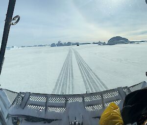 Inside a snow groomer looking out on to snow with distant icebergs on the horizon