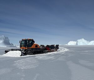 A snow groomer at work with icebergs in the background