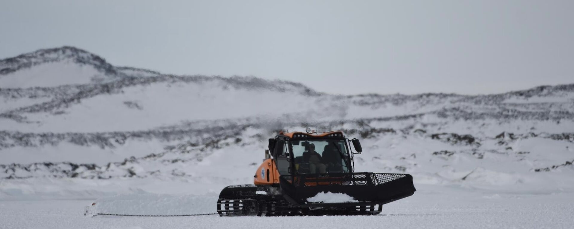 A yellow and black snow groomer at work on the sea ice