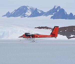 small plane lands on sea ice, with ice plateau and mountains in background