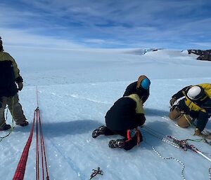 Three people sitting on ice changing climbing lines while one person looks on