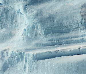 Three adult emperor penguins at the base of a large iceberg