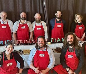 Group of people standing around the dessert buffet all wearing red aprons