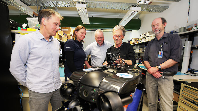 Five people gathered around a remotely operated vehicle in an electronics laboratory.