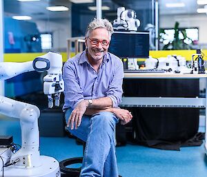 A man sitting beside a robotic arm in a laboratory.