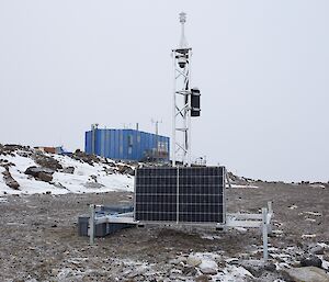 Automatic weather station with solar panel; blue building in the background