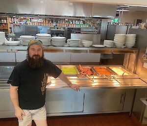 A man wearing a bandana standing in front of a stainless steel self-serve counter, with bain-maries filled with meat and vegetables he has prepared