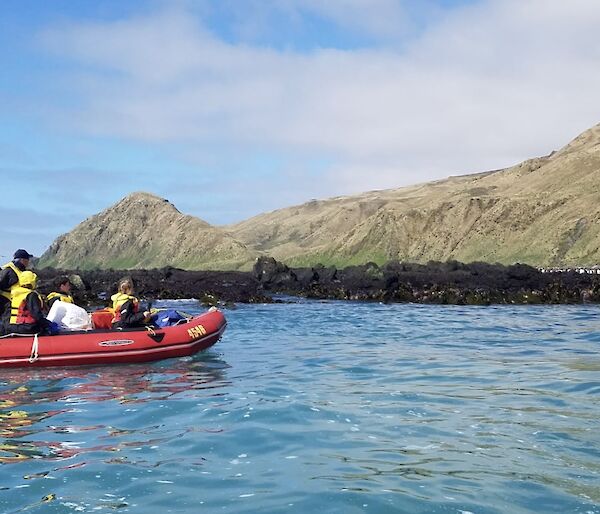 A group of people in a red inflatable boat cruise past the shore of a rocky island