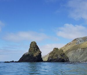 Tow large rocky outcrops stand proud in the water on a blue sky day