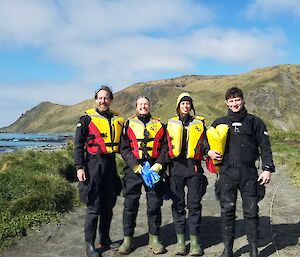 Four people stand onshore in their life jackets as they prepare to go on a boating trip