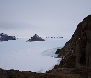 View from above of ice plateau with mountain peaks rising from the ice