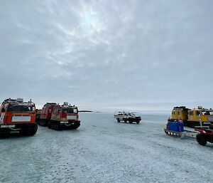 Three Hägglunds, a quad bike and a ute lined up on the sea ice waiting for the plane