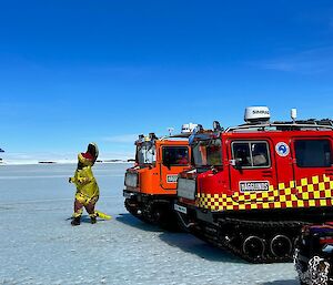 Person in T-Rex costume stands in front of two hagglunds on sea ice