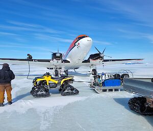 A red and white plane on the sea ice refuelling from equipment nearby
