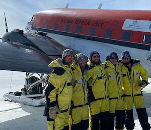 Expeditioners in yellow survival gear standing in front of a red and white aircraft