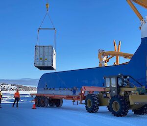 Discharging cargo from a blue ship via a crane onto a trailer pulled by a large tractor