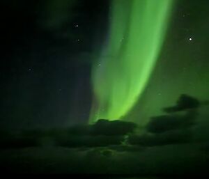 A beautiful green aurora peaks out from behind some clouds in the night sky