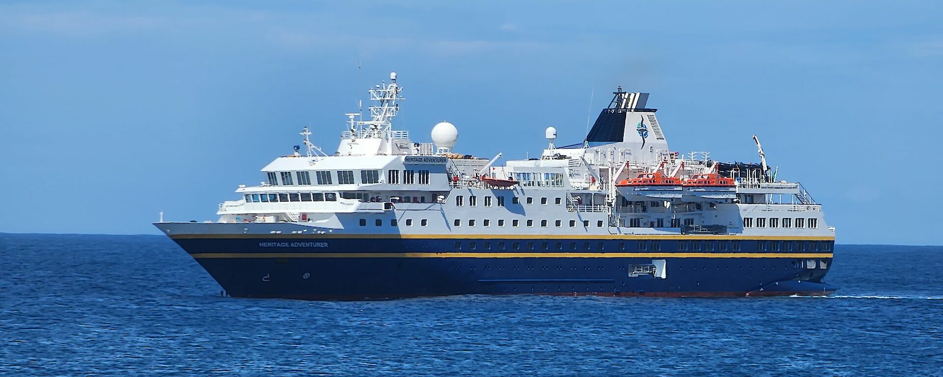 A large blue and white cruise ship sits on the blue ocean