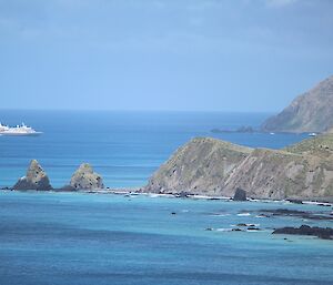 A blue and white cruise ship sits off the rugged green coast line