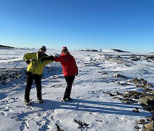 Two smiling women with elbows touching. Sea-ice and icebergs in the background