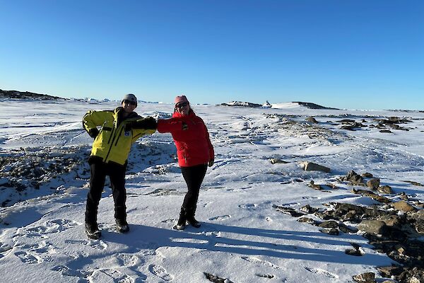 Two smiling women with elbows touching. Sea-ice and icebergs in the background