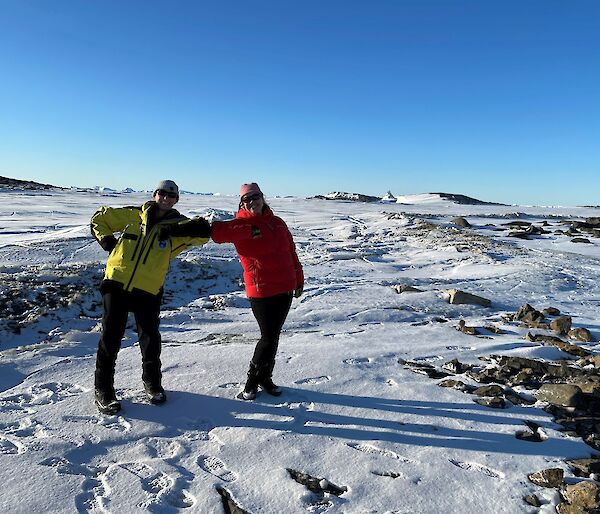 Two smiling women with elbows touching. Sea-ice and icebergs in the background