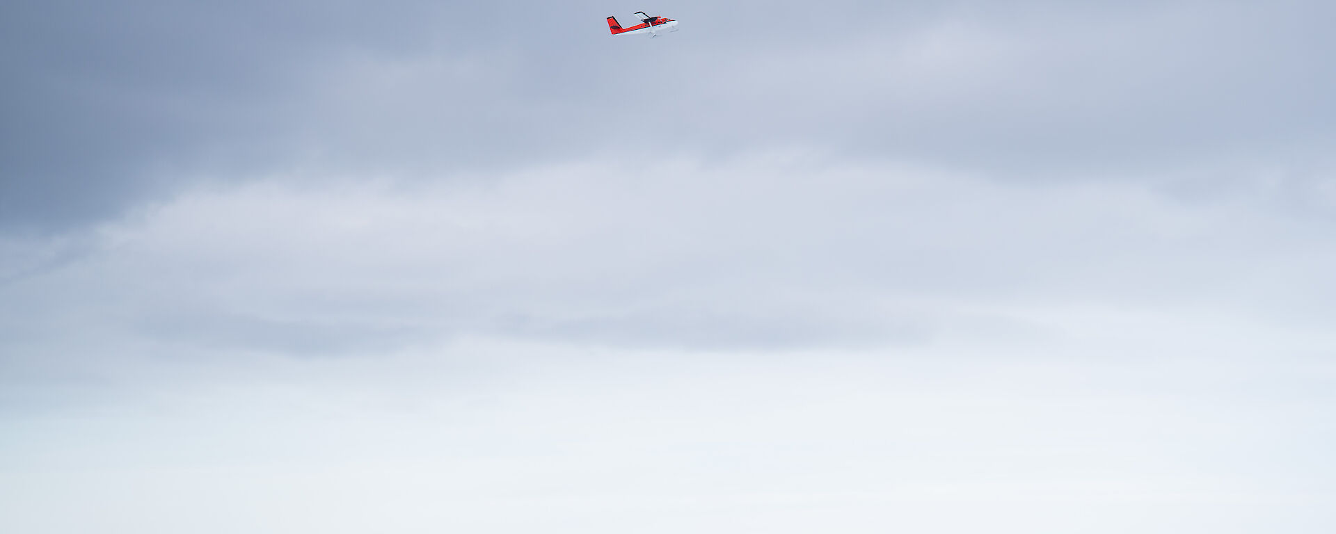 A small red plane flying above buildings in a snowy landscape