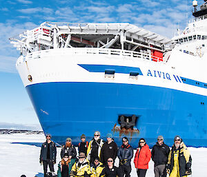 Group of smiling people in front of a blue icebreaker in the sea-ice