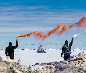 Two people setting off flares to farewell a blue icebreaker in the background