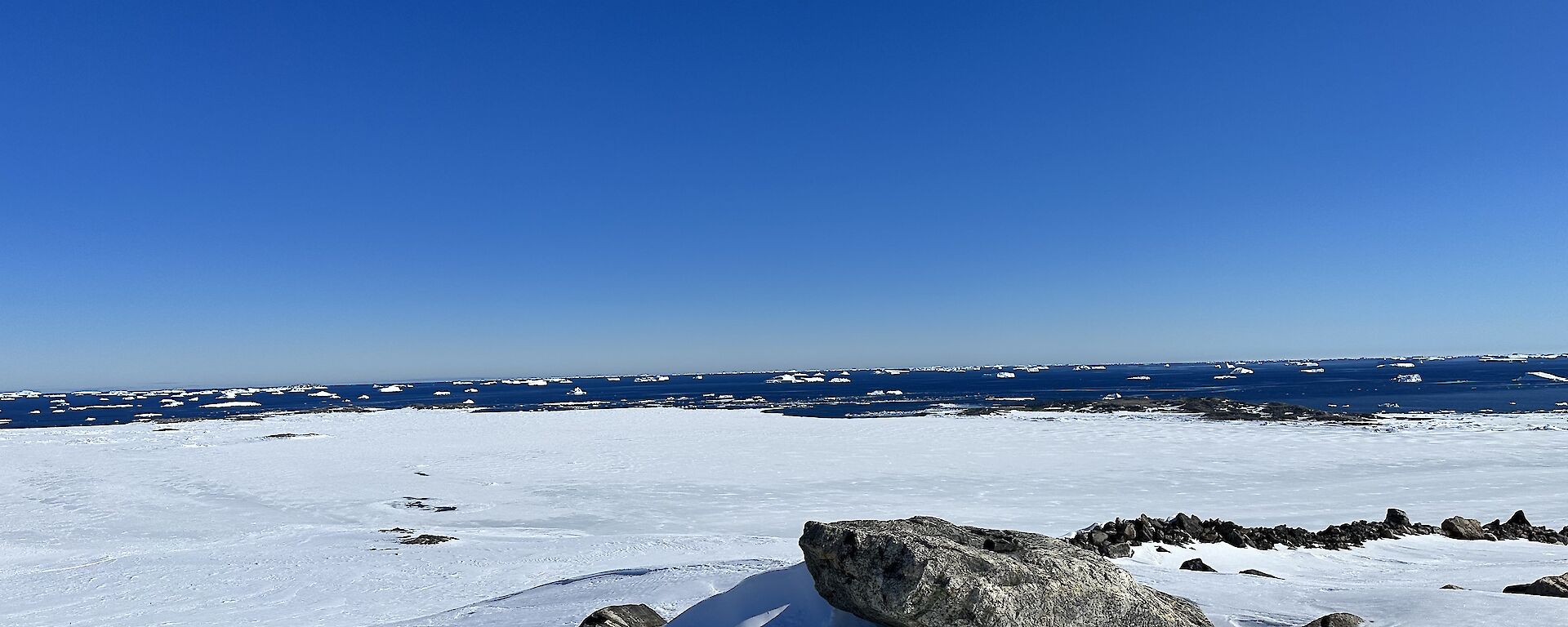 Snow covered mountain with boulders in foreground and a bright blue sky