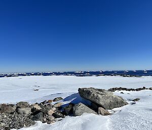 Snow covered mountain with boulders in foreground and a bright blue sky