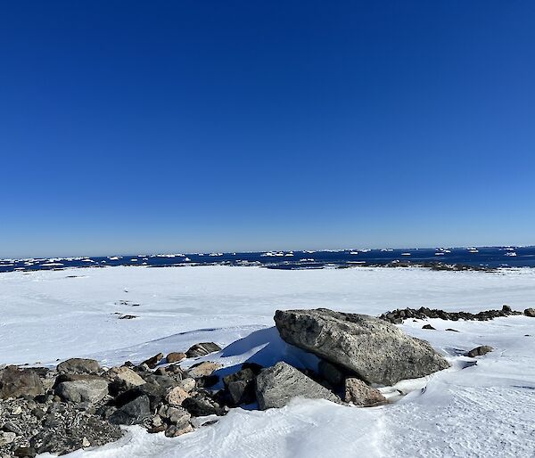 Snow covered mountain with boulders in foreground and a bright blue sky
