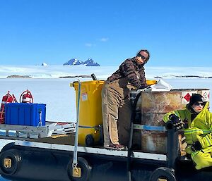 Two people rest on a refuelling trailer enjoying the sun on the ice