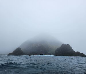 A rocky outcrop is surrounded in fog